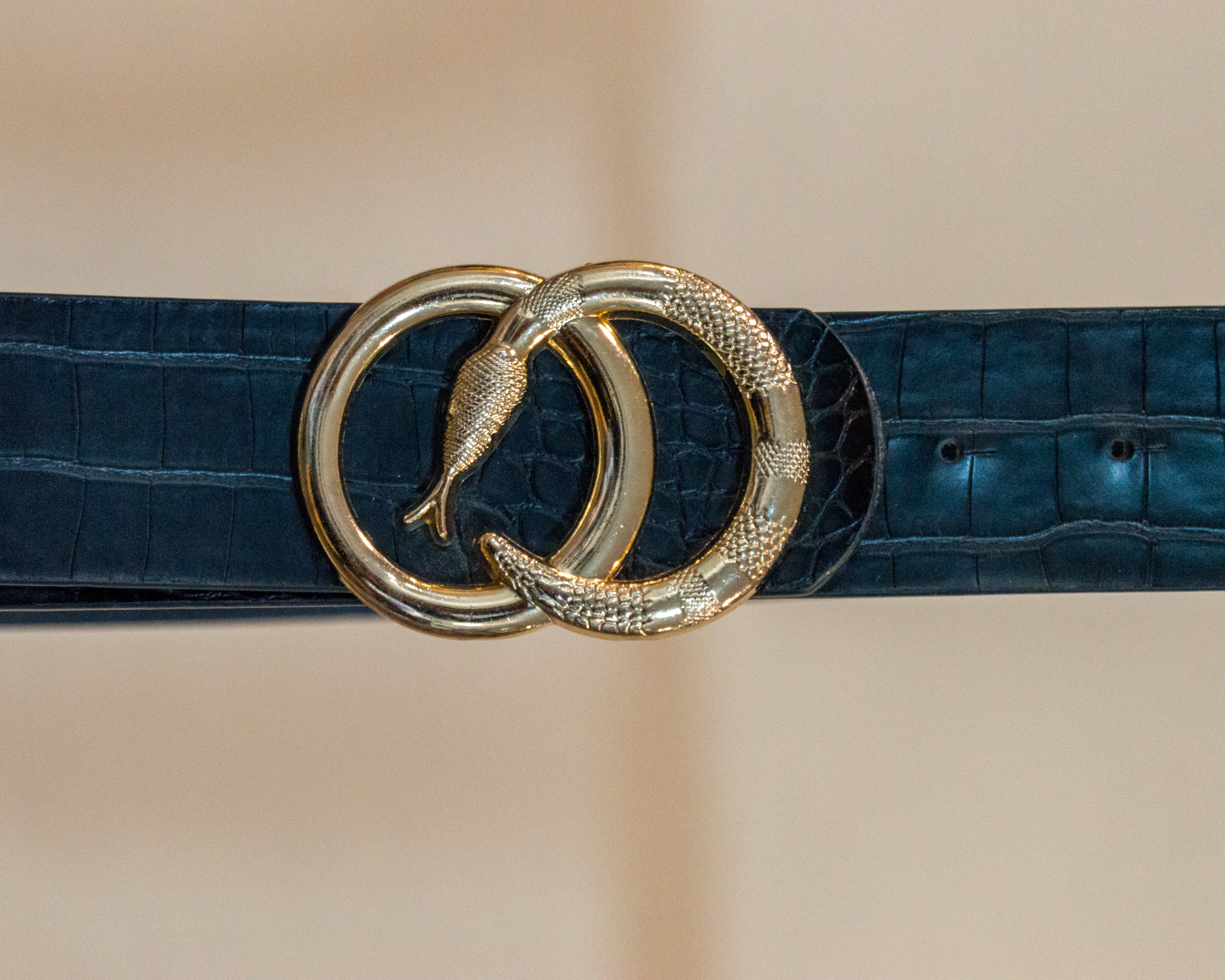 black belt with a gold snake-shaped buckle on a beige background