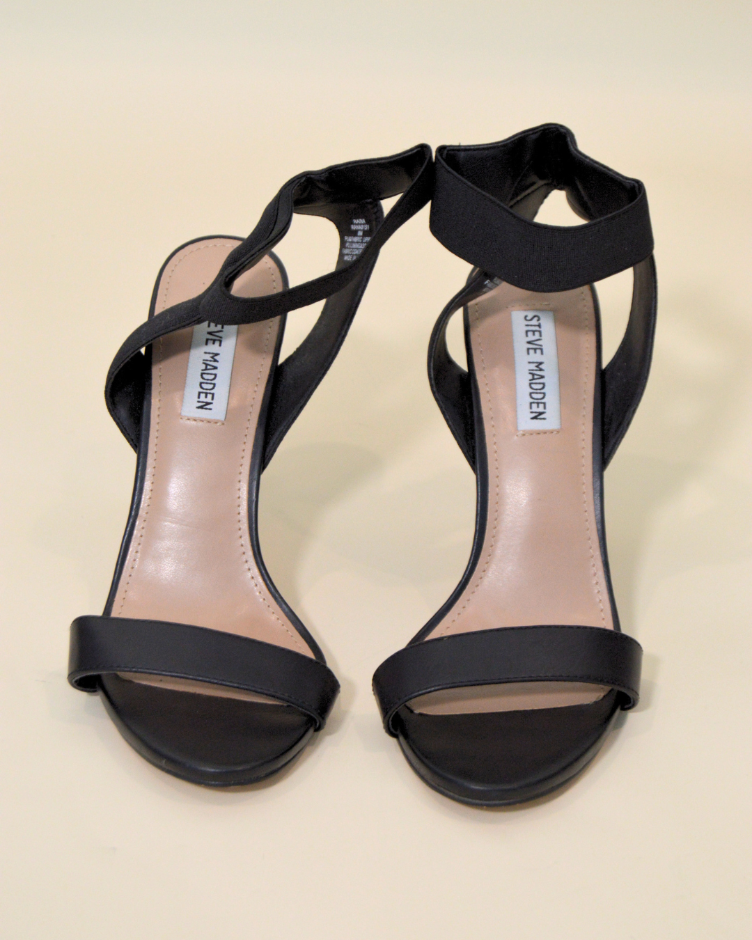 Black high-heeled sandals with 'Steve Madden' branding on a beige background