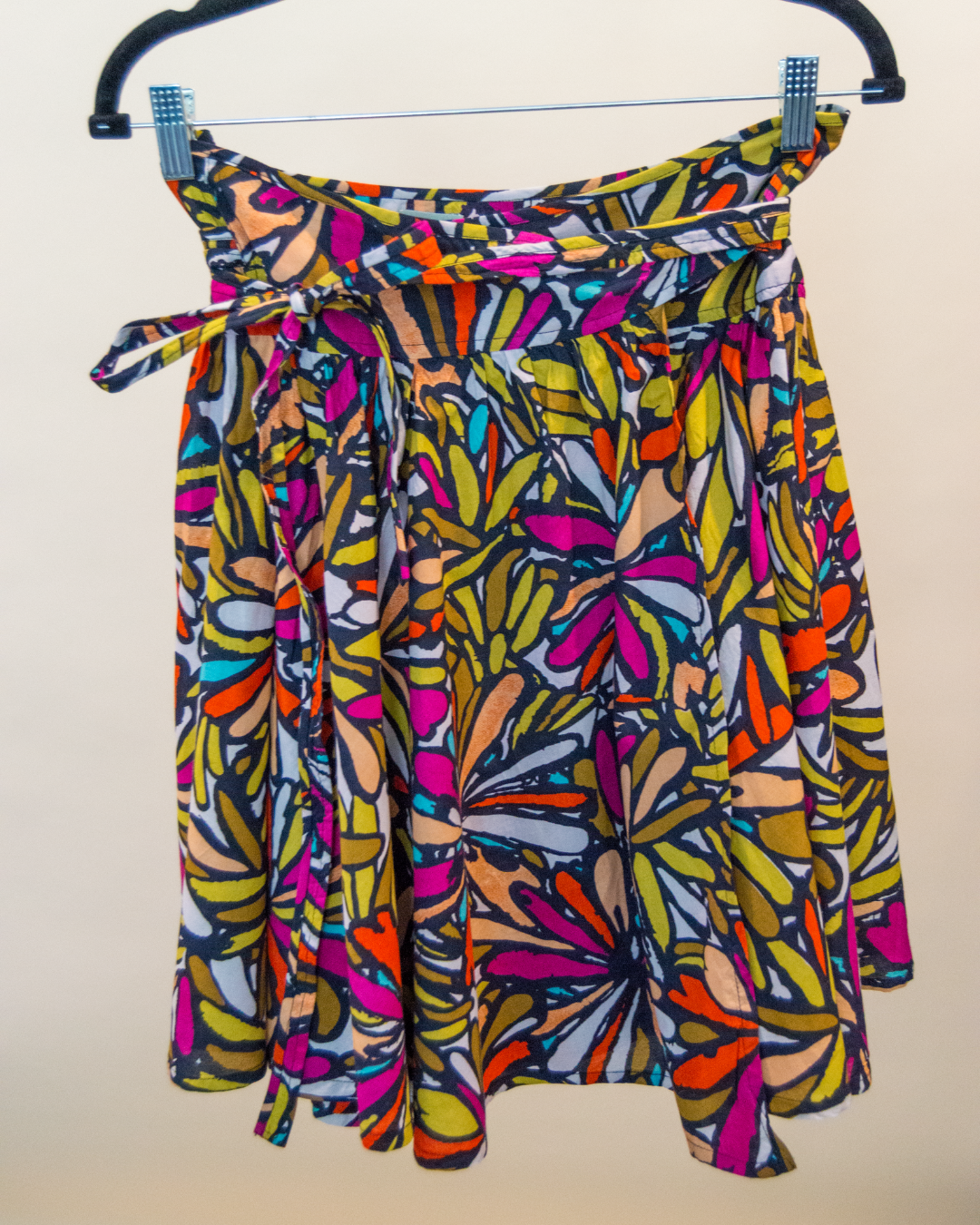 Colorful patterned skirt on a hanger against a plain background