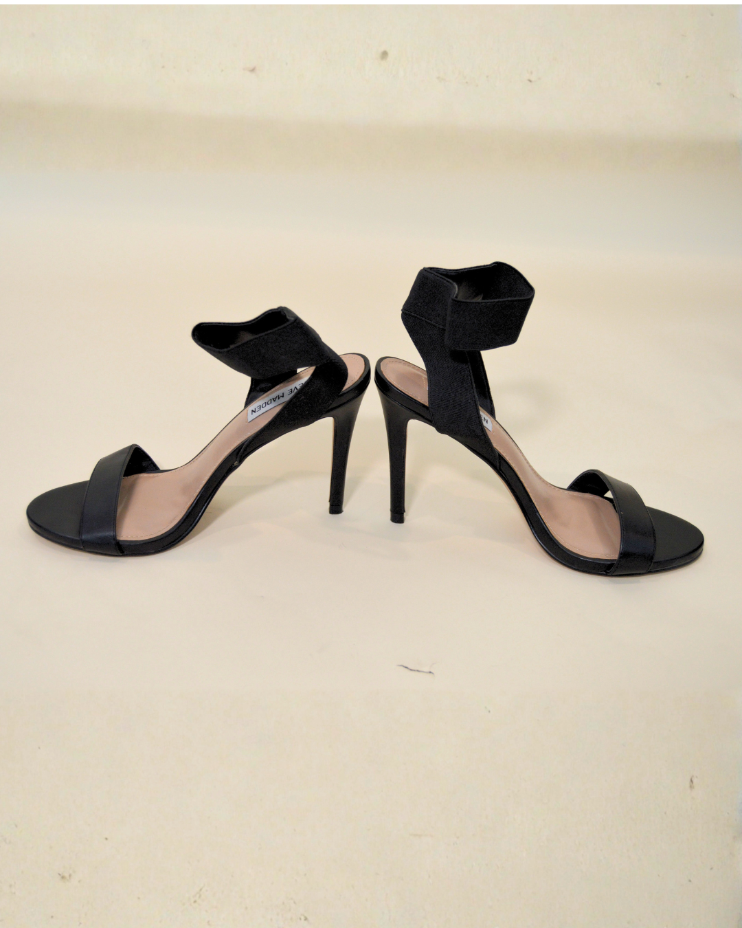 Black high-heeled sandals on a beige background