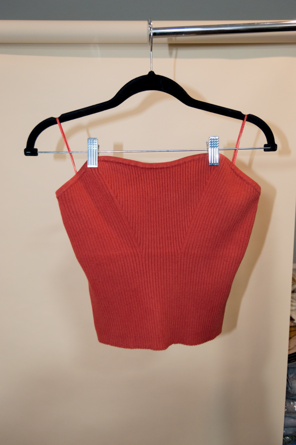 Red ribbed crop top on a hanger against a beige wall.