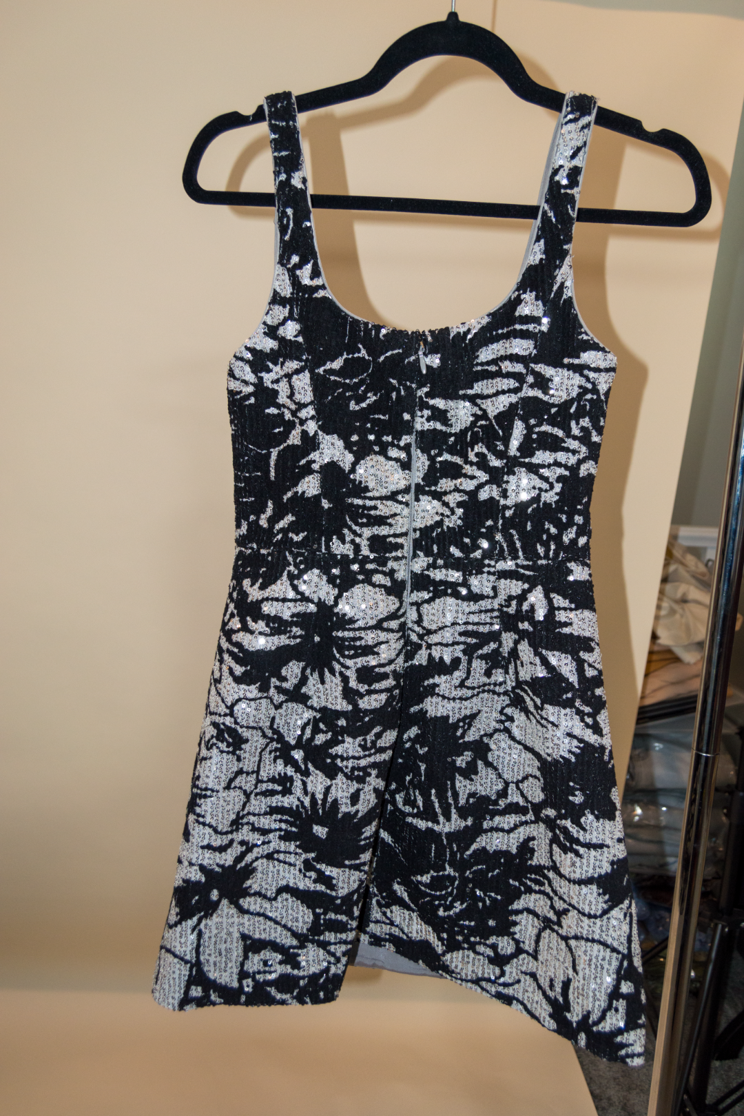 Black and white floral patterned dress on a hanger against a beige wall.