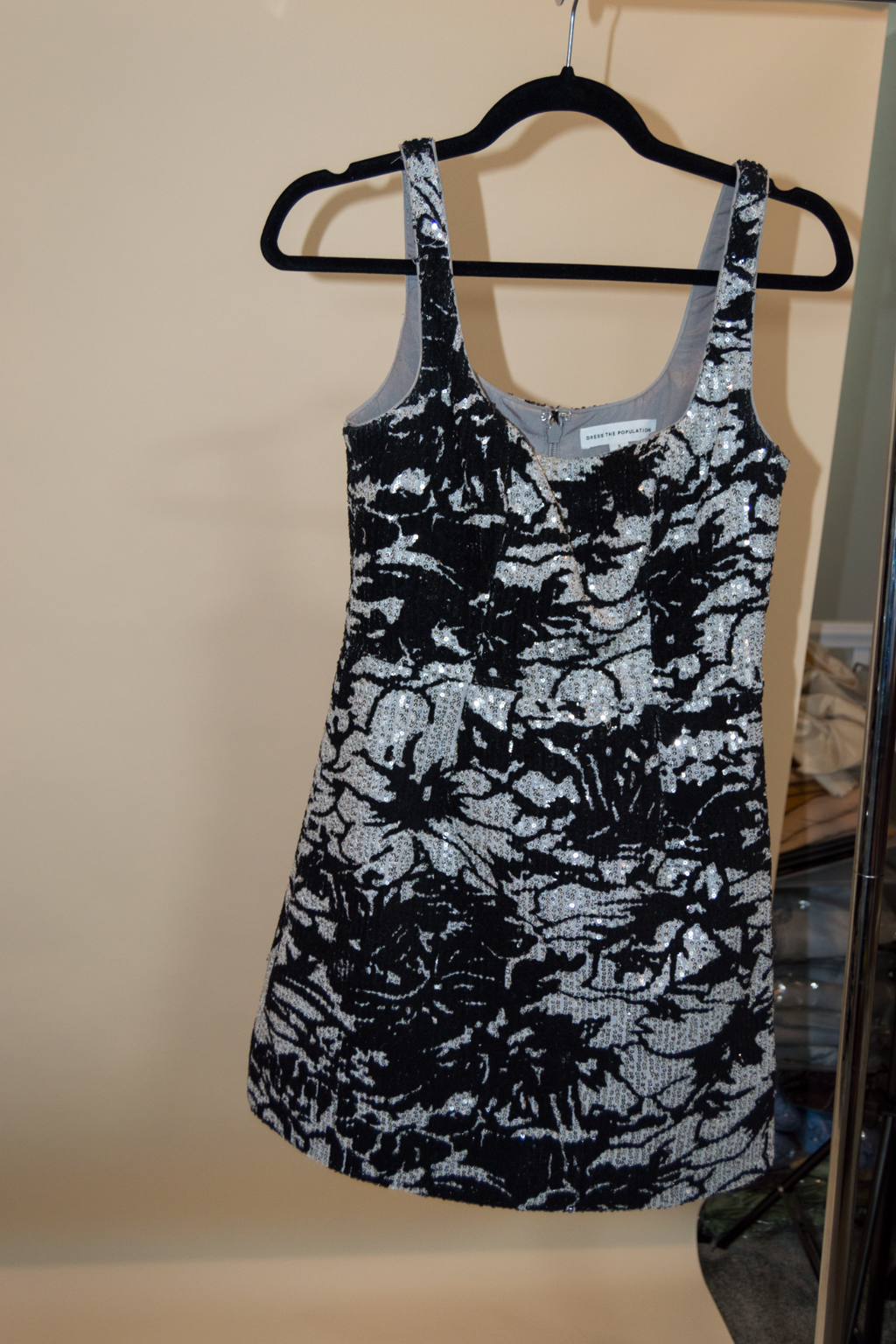 Black and silver floral tank top on a hanger against a beige wall.