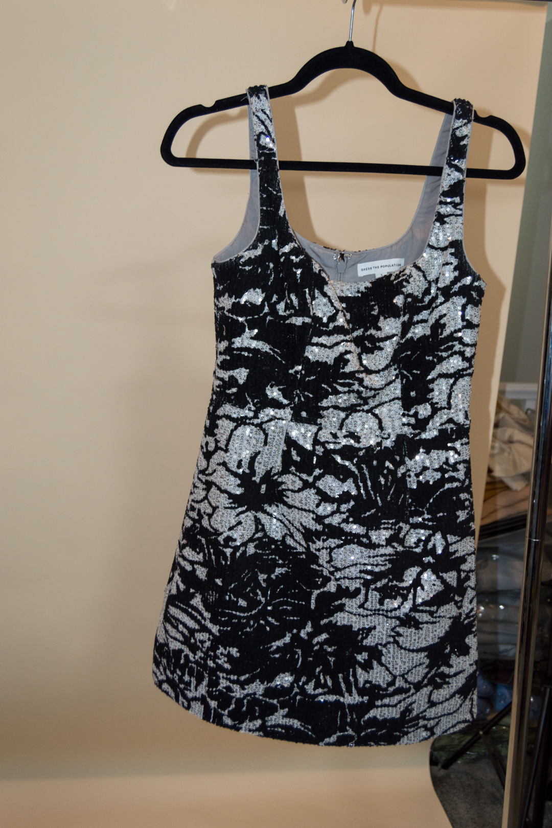 Black and silver floral tank top on a hanger against a beige wall.