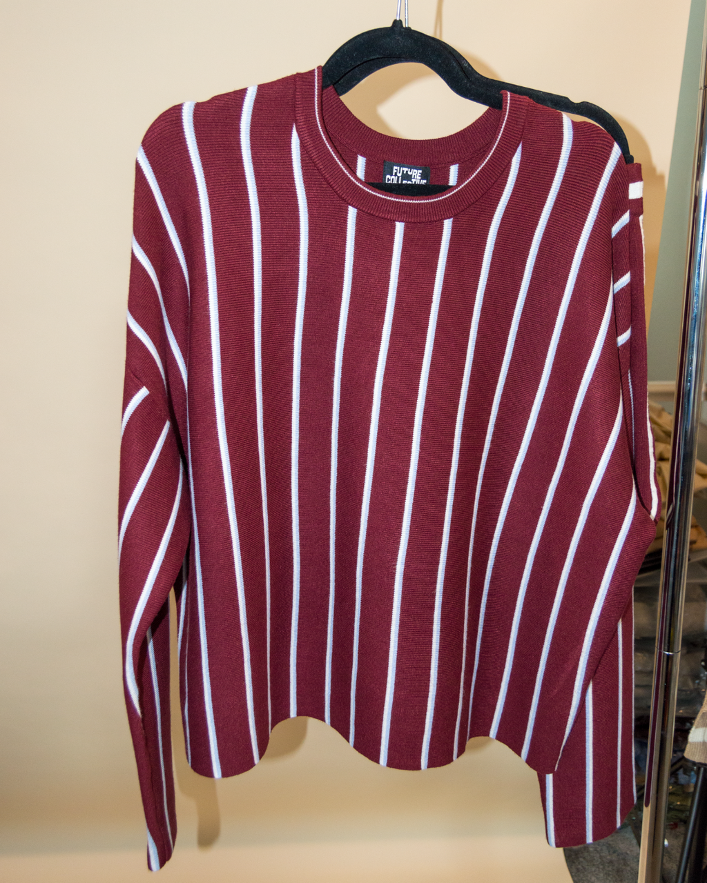 Maroon and white striped shirt on a hanger against a beige wall.