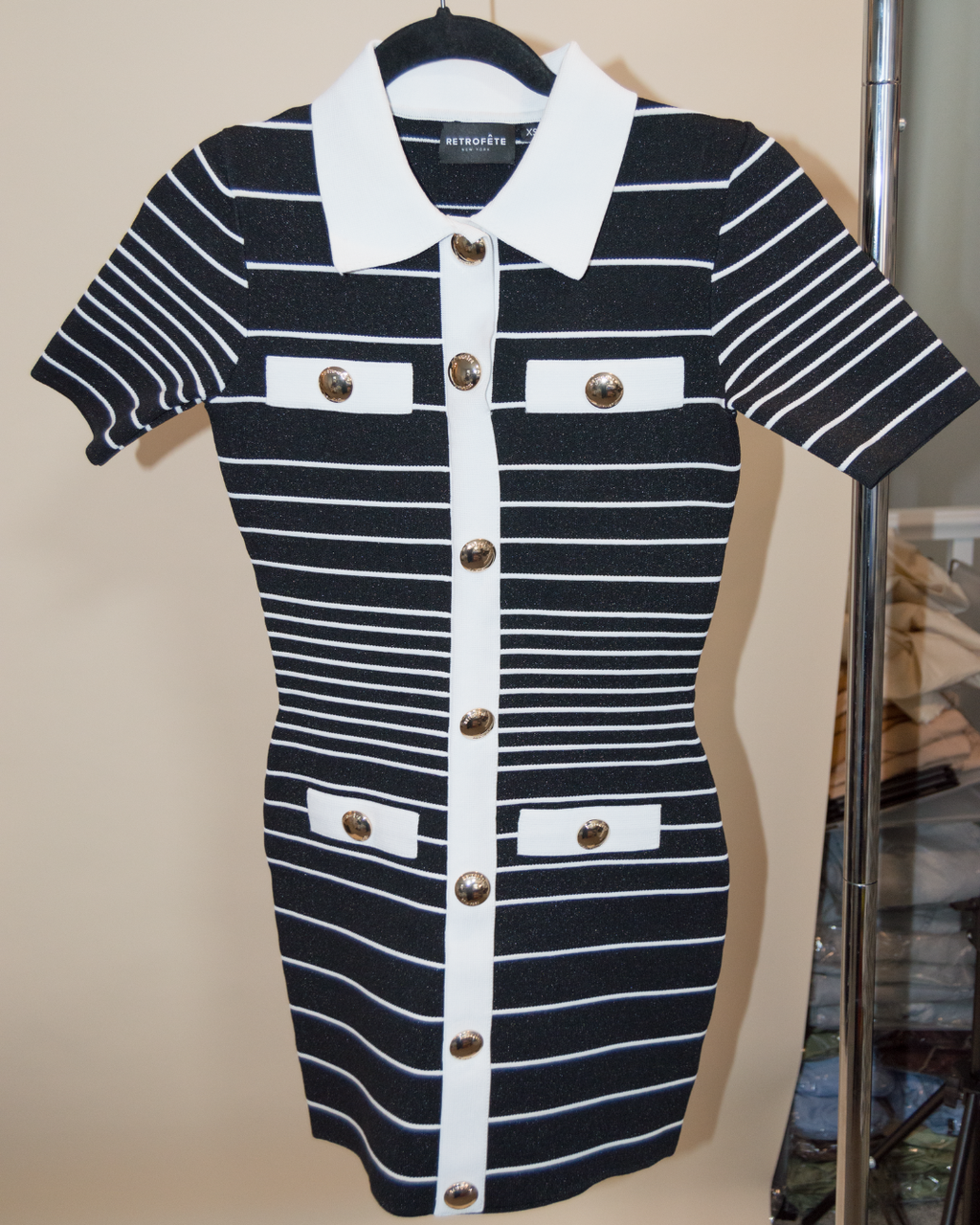 Black and white striped dress with button details on a hanger against a beige wall.