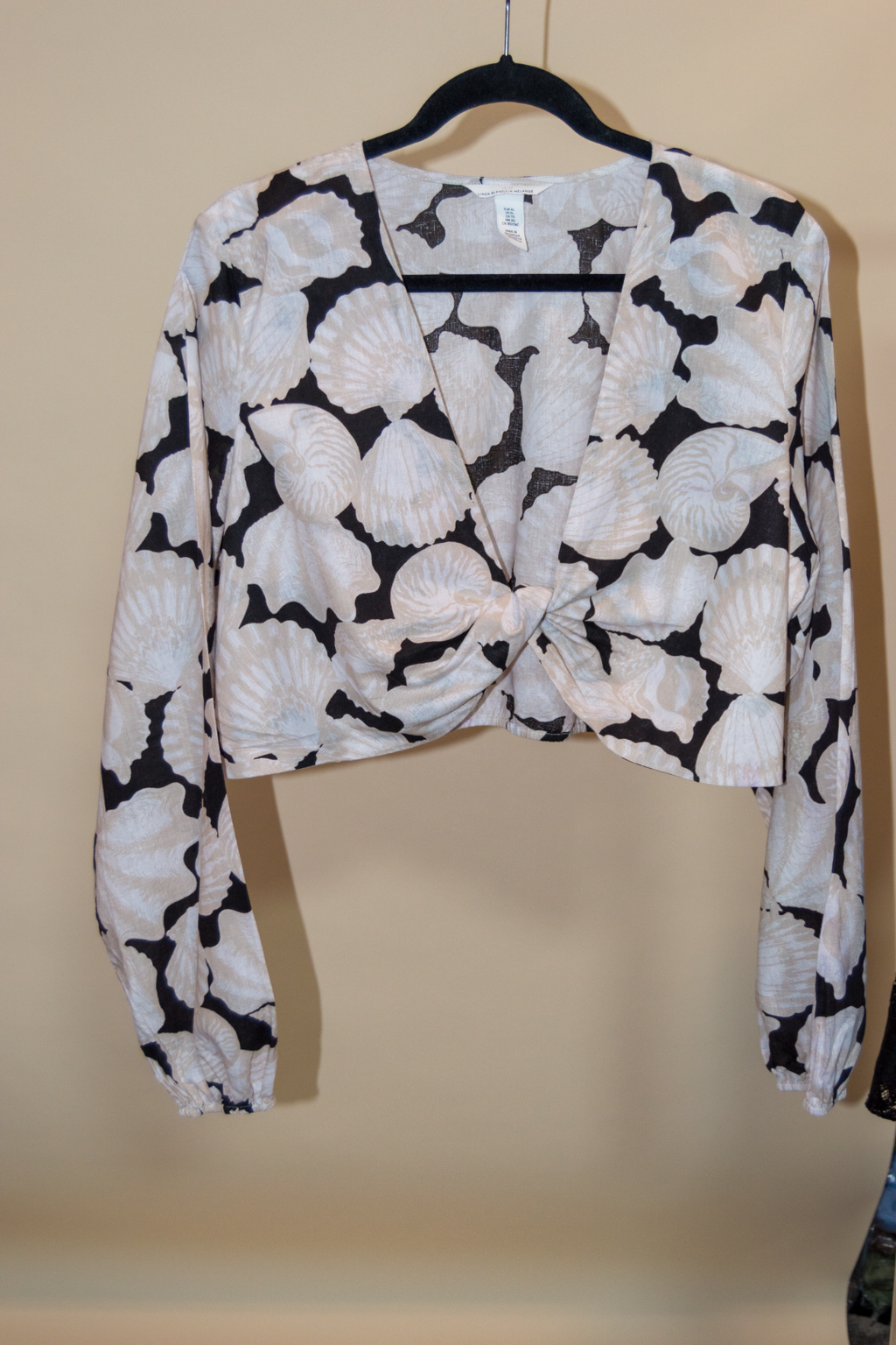 Black and white patterned long-sleeve top on a hanger against a beige background